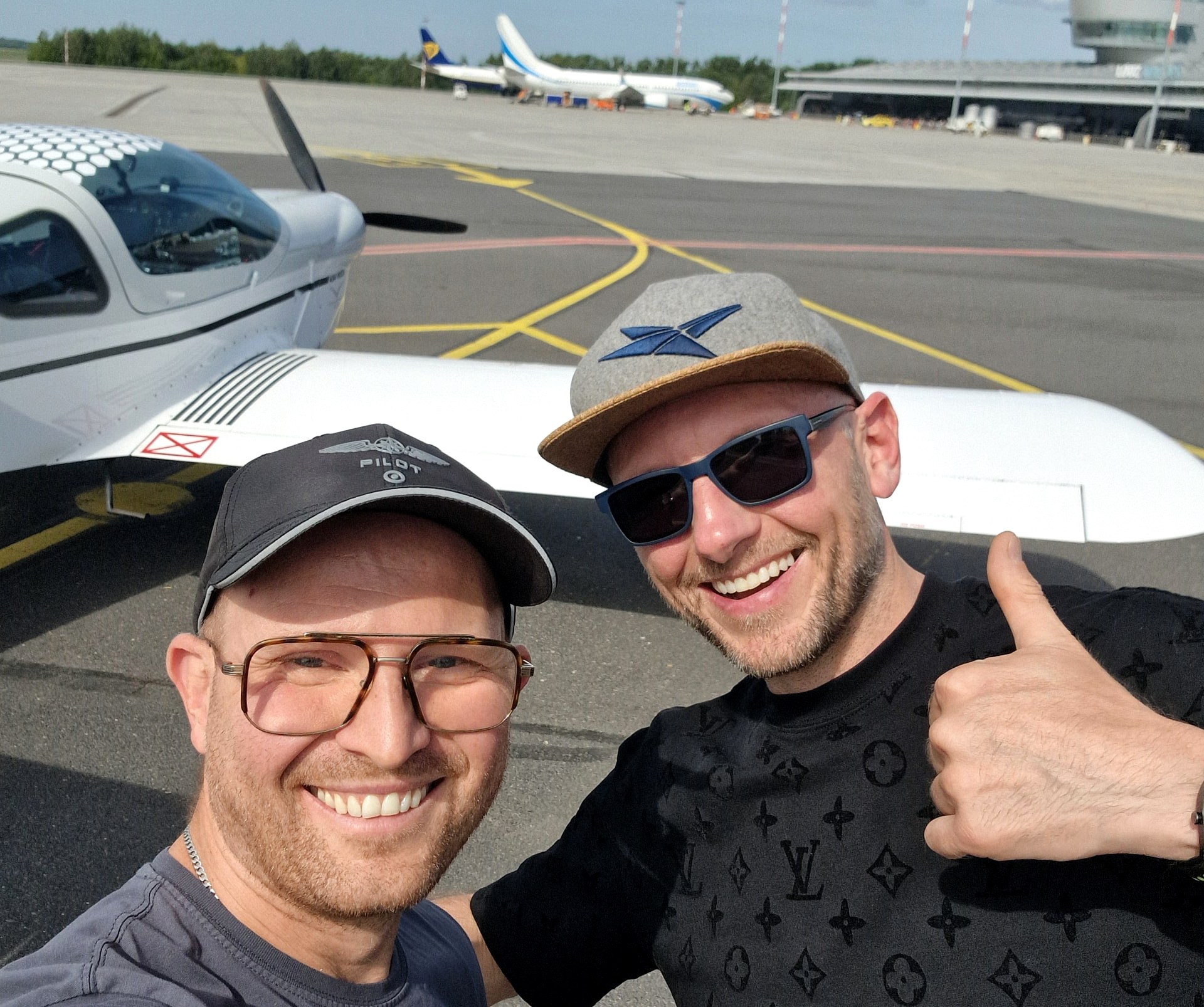 Pilot i pasażer uśmiechnięci przy małym samolocie na płycie lotniska